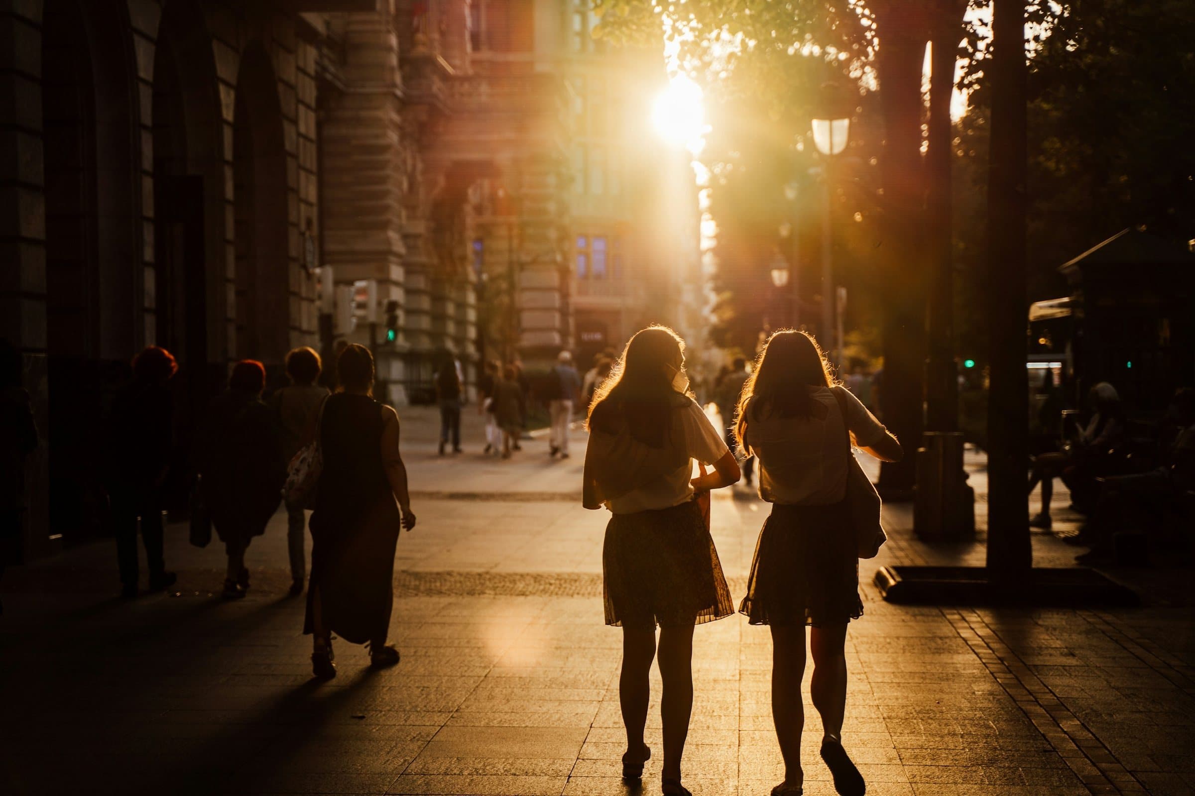 Two friends walking into the evening light on a city street